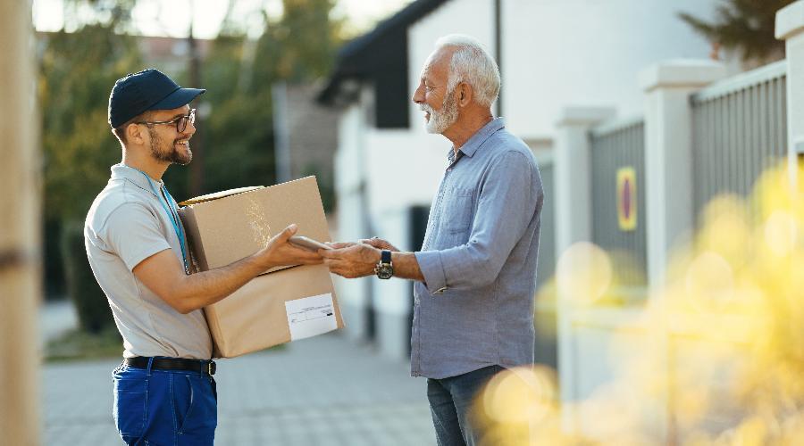 An elderly man signing his package and smiling at a happy delivery guy