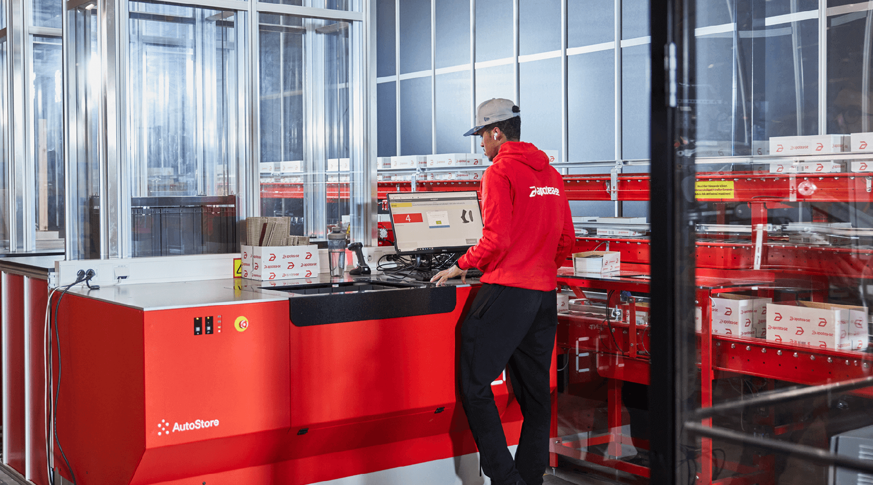A warehouse worker in Apotea at a red AutoStore workstation