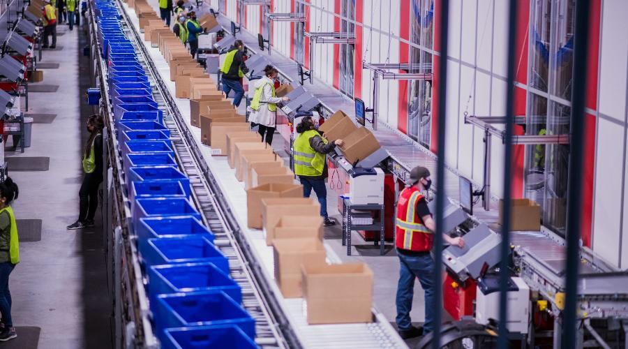 A PUMA warehouse with warehouse workers lined up working next to conveyor technology integrated with AutoStore