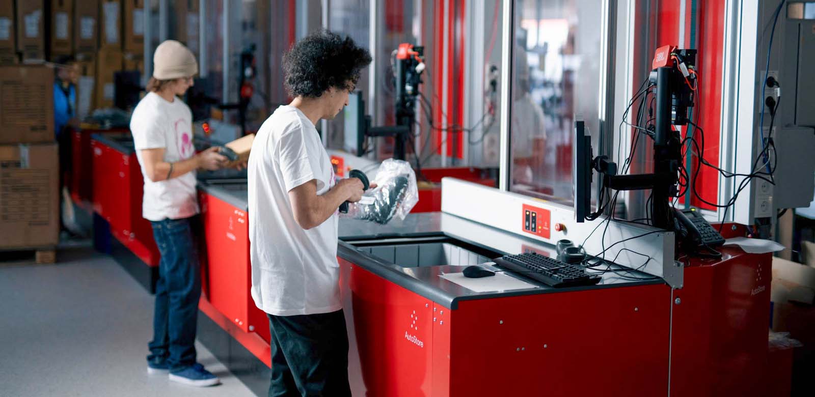 Two warehouse workers picking and fulfilling orders at two AutoStore workstations