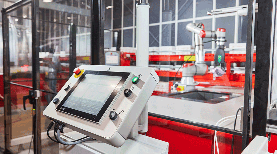 Robotic arm picking items from AutoStore behind computer screen. Image.