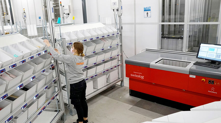 Arvato worker carrying items from AutoStore Port to put cart.