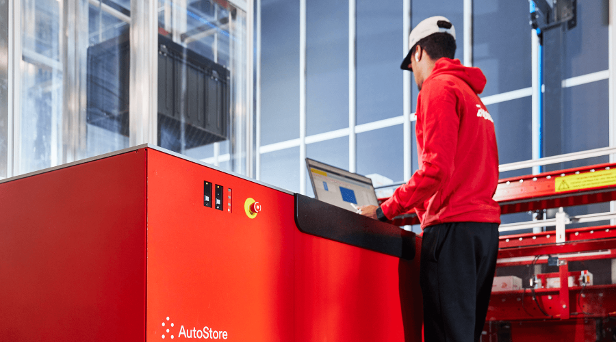 Warehouse worker at a red AutoStore workstation looking at a screen