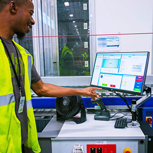 Best Buy employee filling product order at an AutoStore system workstation. Image.
